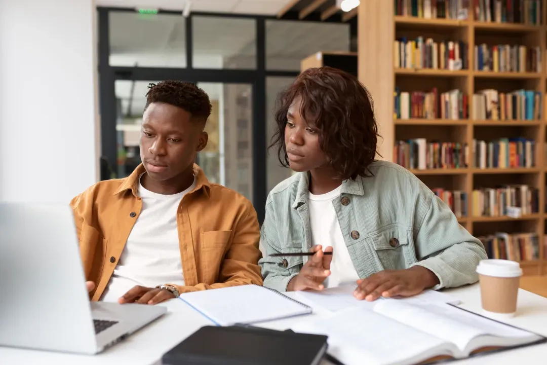 Two students collaborating on a laptop in a library